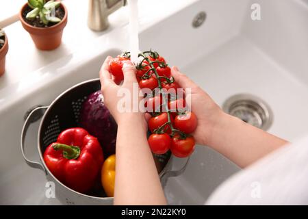 Woman washing fresh cherry tomatoes in kitchen sink, closeup Stock Photo