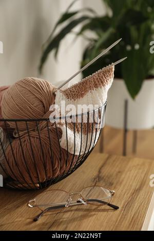 Glasses, yarn balls and knitting needles on wooden table indoors. Creative hobby Stock Photo