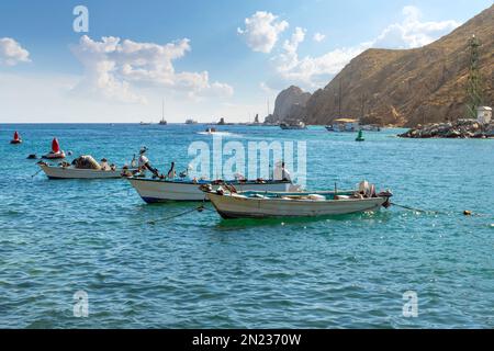Pelicans enjoy relaxing on fishing boats in the sun with the El Arco coastline behind at the port of Cabo San Lucas, Mexico. Stock Photo