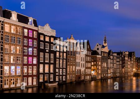 AMSTERDAM, THE NETHERLANDS - JANUARY 18, 2023: Cityscape of traditional Dutch houses during blue hour at the Damrak canal in Amsterdam Stock Photo