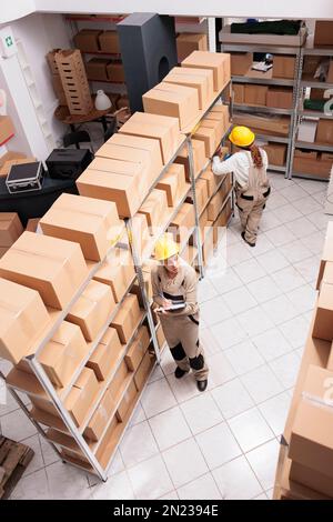 Retail store warehouse workers packing boxes and supervising goods inventory. Two women wearing protective helmets and overalls working in ecommerce shop storehouse top view Stock Photo