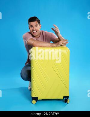 Excited man with suitcase for summer trip on blue background. Vacation travel Stock Photo
