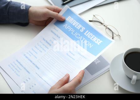 Man with driver's license application form and cup of coffee at white table, closeup Stock Photo