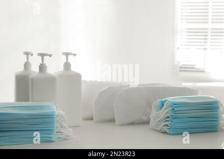 Hand sanitizers and respiratory masks on white table indoors. Protective essentials during COVID-19 pandemic Stock Photo
