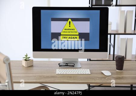 Computer with warning about virus attack on screen in office Stock Photo