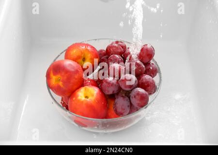 Washing fresh grapes and nectarines in bowl under tap water Stock Photo