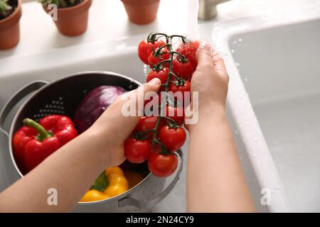 Woman washing fresh cherry tomatoes in kitchen sink, closeup Stock Photo