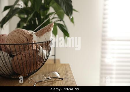 Glasses, yarn balls and knitting needles on wooden table indoors, space for text. Creative hobby Stock Photo