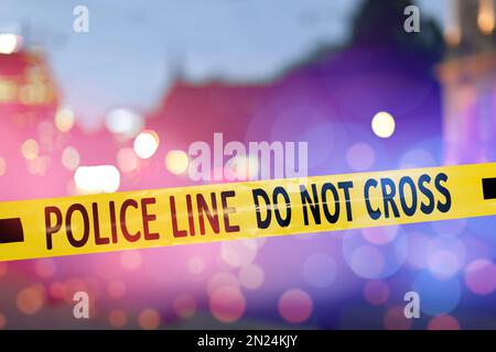 Yellow law enforcement tape isolating crime scene. Blurred view of city, toned in red and blue police car lights Stock Photo