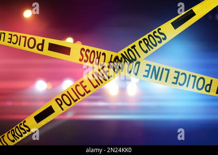 Yellow law enforcement tape isolating crime scene. Blurred view of city street, toned in red and blue police car lights Stock Photo