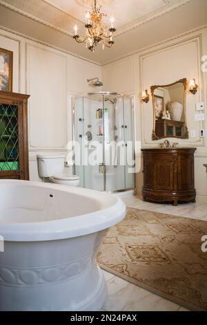 Freestanding boat style bathtub, glass shower stall and wooden vanity in master bathroom on upstairs floor inside Renaissance style home. Stock Photo