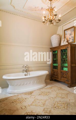 Freestanding boat style bathtub and wooden cabinet with leaded glass panels in master bathroom on upstairs floor inside Renaissance style home. Stock Photo