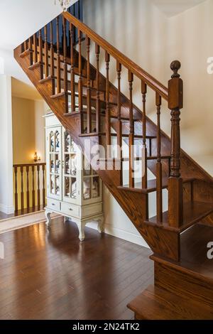 Wooden linen cabinet with glass paneled doors on oak wood hardwood floor under brown stained oak wood stairs inside reproduced Renaissance style home. Stock Photo