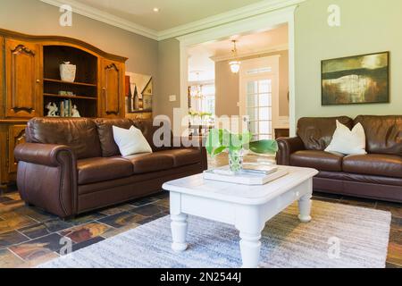 White wooden coffee table with brown leather sofas and wooden buffet in living room with earth tone slate flooring inside contemporary style home. Stock Photo