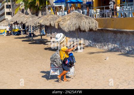 A Mexican man sells and wears hats along the sandy beach at the Golden Zone of Mazatlan, Mexico. Stock Photo