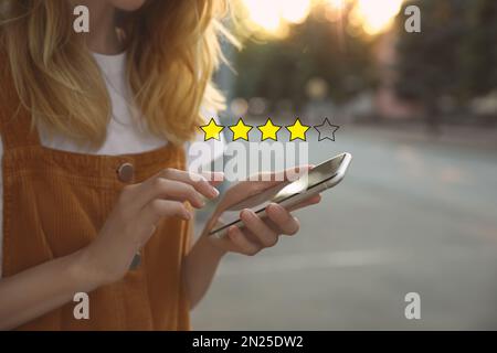 Woman leaving review online via smartphone outdoors, closeup. Four out of five stars over gadget Stock Photo