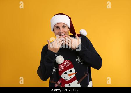 Surprised man in Christmas sweater and Santa hat on yellow background Stock Photo