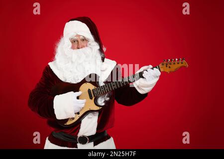 Santa Claus playing electric guitar on red background. Christmas music Stock Photo