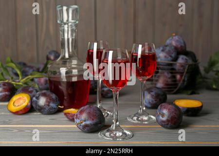 Delicious plum liquor and ripe fruits on grey wooden table. Homemade strong alcoholic beverage Stock Photo