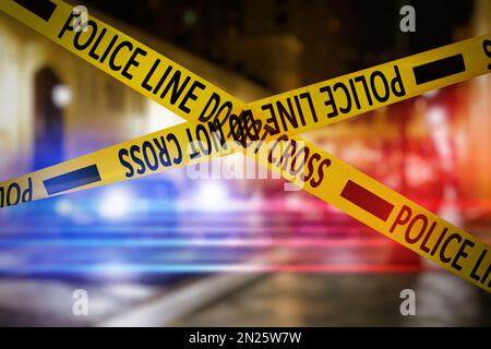 Yellow law enforcement tape isolating crime scene. Blurred view of city street, toned in red and blue police car lights Stock Photo