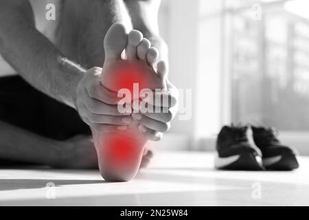 Man suffering from foot pain on floor indoors, closeup Stock Photo