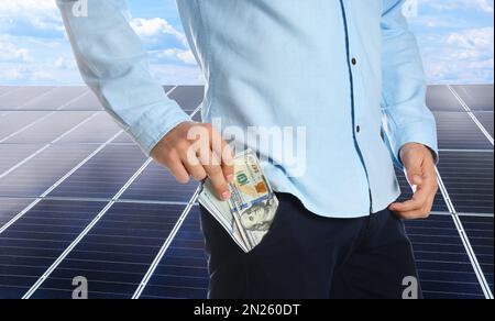 Man with money and installed solar panels on background, closeup. Economic benefits of renewable energy Stock Photo