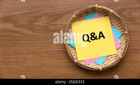 Top view of a basket fill with colorful paper and yellow paper written with Q and A on a wooden background with copy space. Stock Photo