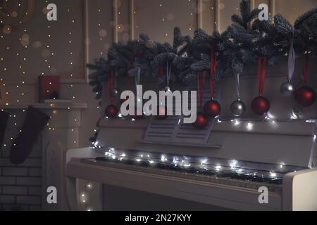 White piano with festive decor and note sheets indoors. Christmas music Stock Photo