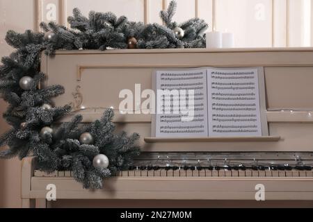 White piano with festive decor and note sheets indoors. Christmas music Stock Photo