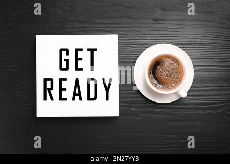 Card with text Get Ready and cup of coffee on dark wooden table, flat lay Stock Photo