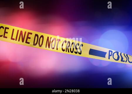 Yellow law enforcement tape isolating crime scene. Blurred background with red and blue police car lights Stock Photo