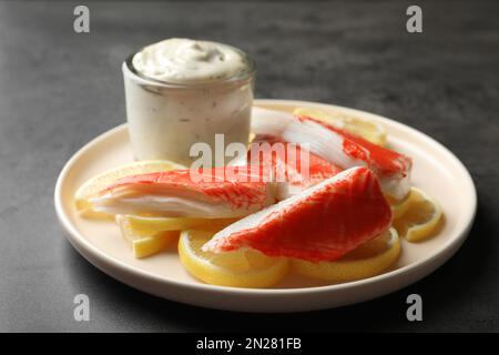 Delicious crab sticks with lemon slices and sauce on grey table Stock Photo