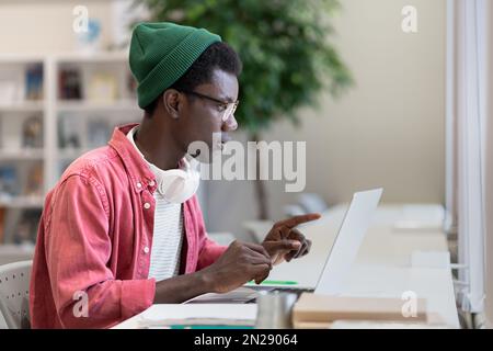 Concentrated self-sufficient African American man sits at table with laptop doing distance learning Stock Photo