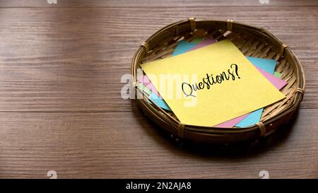 Selective focus of a basket fill with colorful paper and yellow paper written with Questions on a wooden background with copy space. Stock Photo