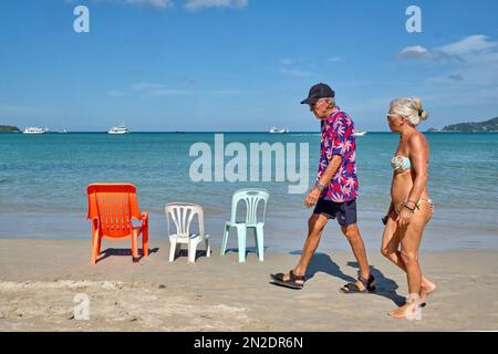 An elderly Western tourist couple walks along Patong Beach, Phuket, Thailand Stock Photo