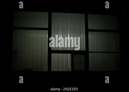 Big window at night. Window in building. Blinds cover light of lamp. House is outside. Stock Photo