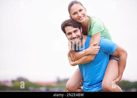 Who needs workout equipment. a young man playfully carrying his girlfriend on his back while working out. Stock Photo
