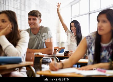 Working her way towards a distinction. A young woman raising her hand as she sits in a varsity class surrounded by her peers. Stock Photo