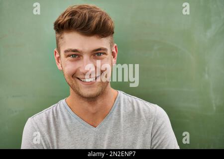 How about a career in teaching. A young man smiling at the camera while standing in front of a blackboard. Stock Photo