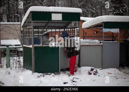 Man is looking for food in garbage. Man looks into dumpster in winter. Poor man on street. Garbage cans in Russia. Stock Photo