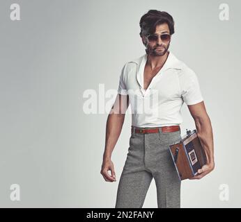 Stepping out with his tunes - 70s style. A studio shot of a handsome man in retro 70s wear holding a cassette player. Stock Photo