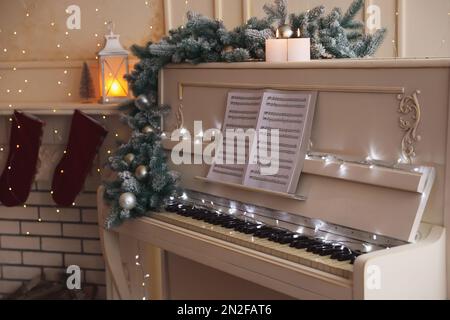 White piano with festive decor and note sheets indoors. Christmas music Stock Photo