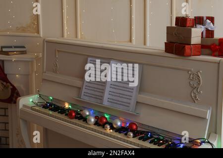 White piano with festive decor and note sheets indoors. Christmas music Stock Photo