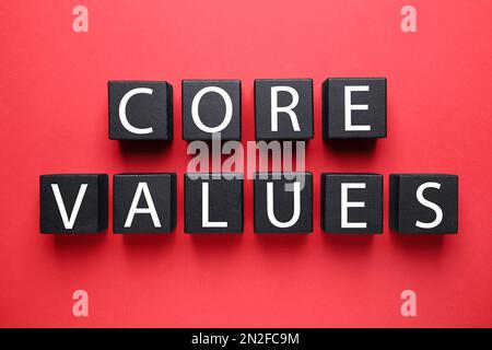 Black wooden cubes with phrase CORE VALUES on red background, flat lay Stock Photo
