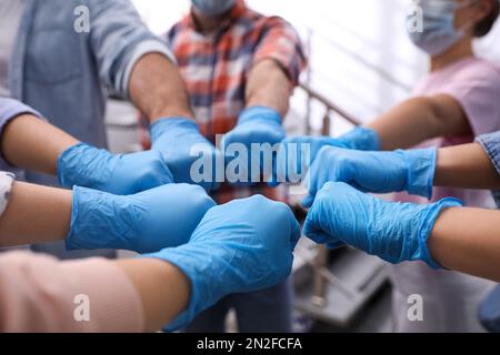 People in blue medical gloves joining fists indoors, closeup Stock Photo