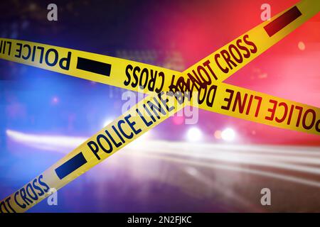 Yellow law enforcement tape isolating crime scene. Blurred view of city street, toned in red and blue police car lights Stock Photo