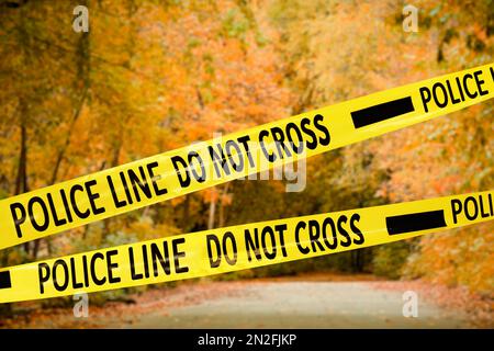 Yellow police tape isolating crime scene. Blurred view of autumn park Stock Photo