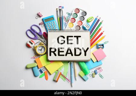 Notebook with text Get Ready surrounded by different stationery on light background, flat lay Stock Photo