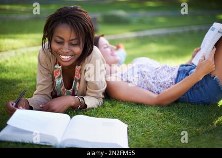Relaxed revision. Two young female students lying on the grass reading. Stock Photo