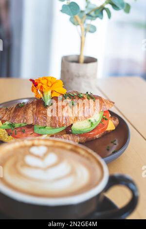 Croissant filled with avocado, tomato and egg on a wooden table in a restaurant Stock Photo